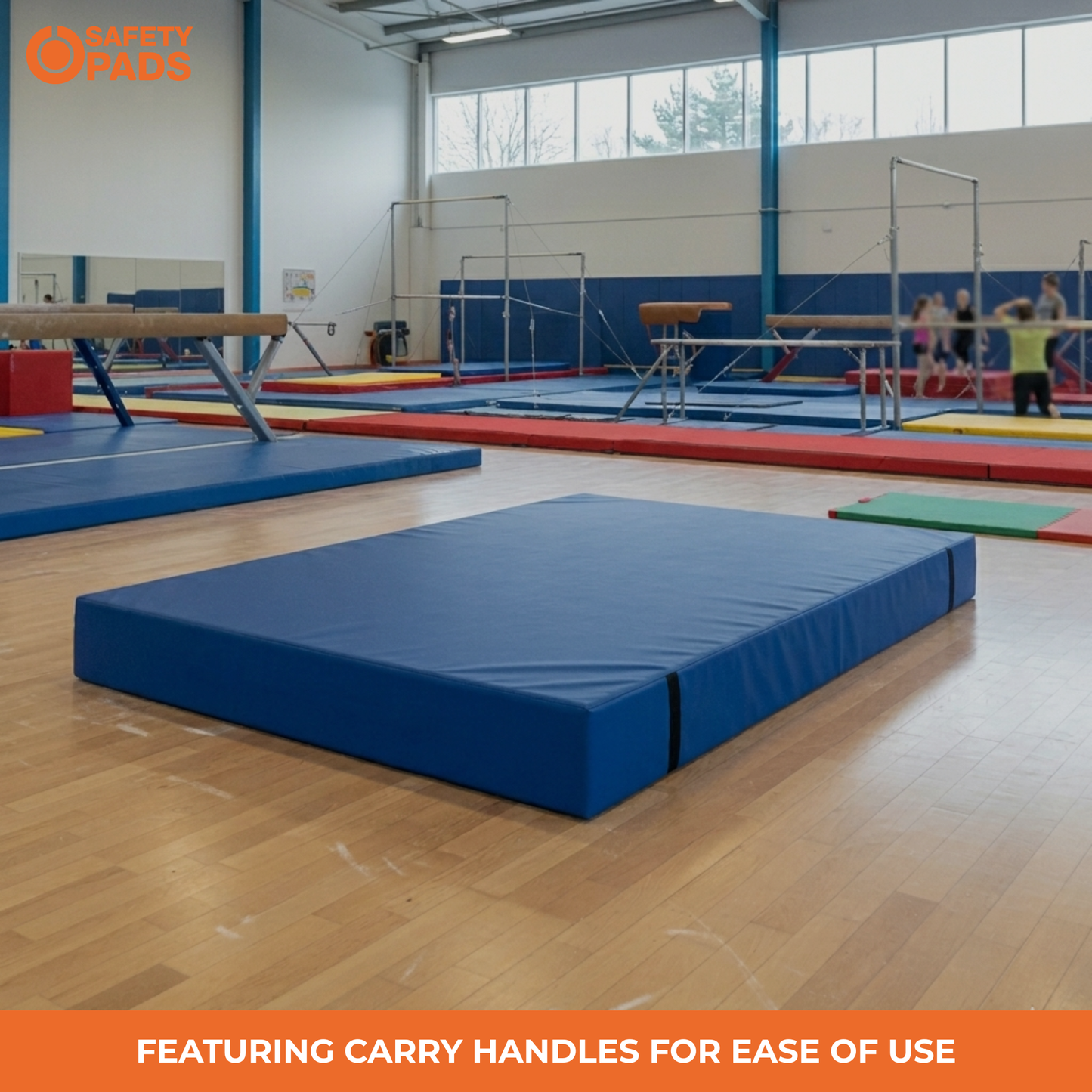 A blue gymnastics floor mat with integrated carry handles on a wooden gym floor, with other gymnastics equipment and a child visible in the background.