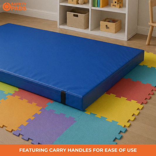 A blue foam play mat with carry handles placed on a colorful interlocking foam floor mat in a child's room. A white storage shelf is visible in the background, and an orange 'Safety Pads' logo appears in the top-left corner with a text banner at the bottom.