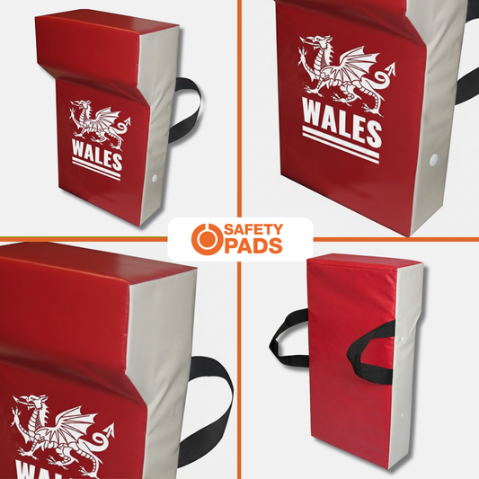 Red and white martial arts safety pad shown in four views, featuring a white Welsh dragon and the word 'WALES' on the front. The pad has black carrying straps and is displayed on a light gray background with an 'SAFETY PADS' logo in the center.