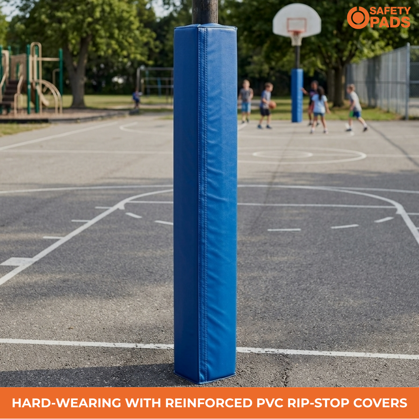 A blue padded safety pad covering a basketball court pole, shown on an outdoor basketball court with children playing in the blurred background. An orange Safety Pads logo is in the top right, and a text banner at the bottom reads 'HARD-WEARING WITH REINFORCED PVC RIP-STOP COVERS'.