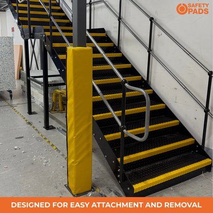 Industrial metal staircase with black steps and yellow safety striping, featuring a yellow protective pad on a post and a silver handrail. The image includes 'SAFETY PADS' branding and an orange banner at the bottom reading 'DESIGNED FOR EASY ATTACHMENT AND REMOVAL'.