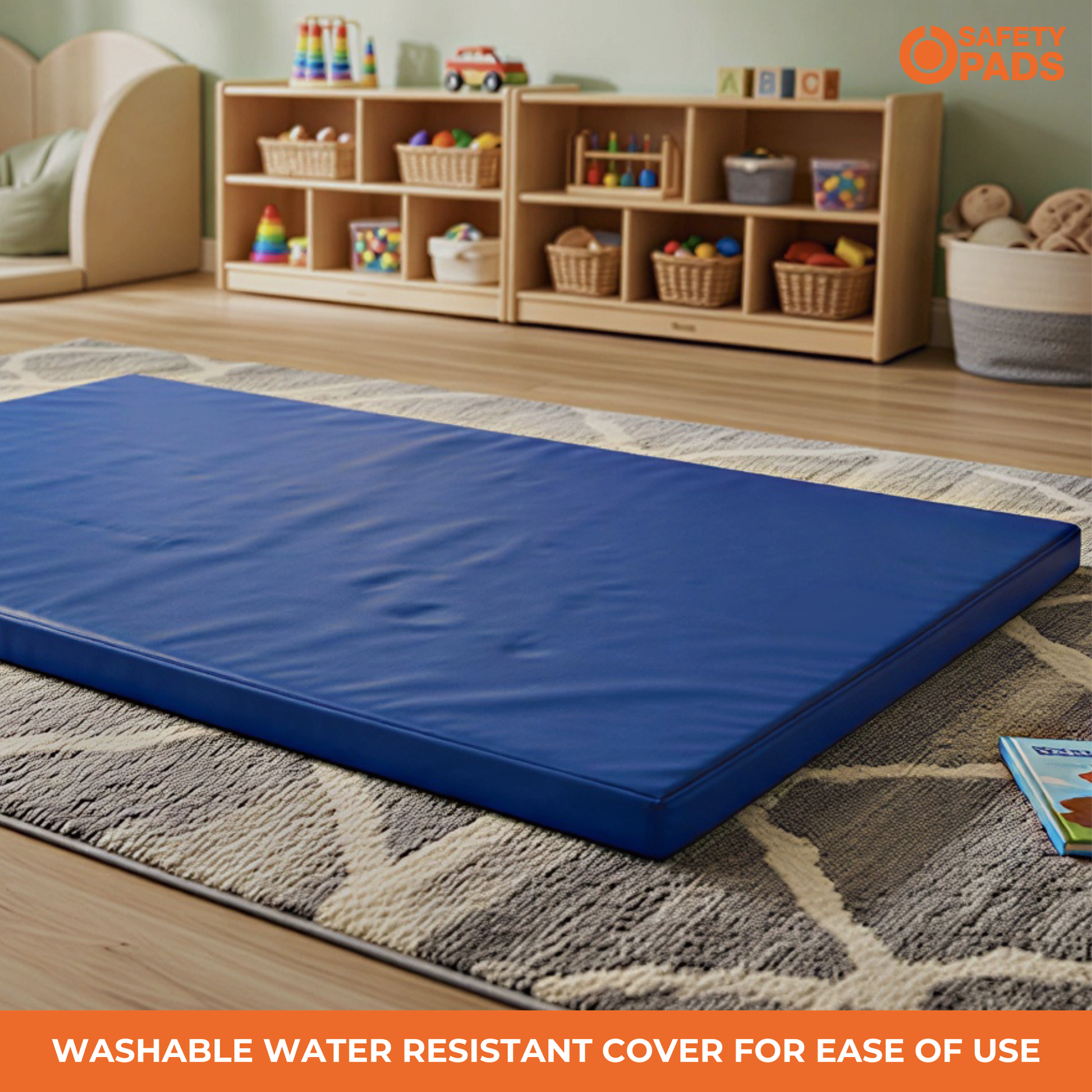 A blue rectangular foam play mat or mattress topper resting on a patterned rug in a children's playroom. The background shows a wooden toy organizer shelf with colorful toys, and an orange 'HEEZEE PADS' logo is visible in the top right corner with an orange text banner at the bottom reading 'WASHABLE WATER RESISTANT COVER FOR EASE OF USE'.