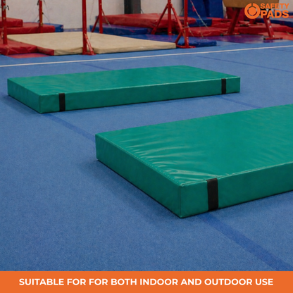 Two green outdoor gymnastics mats on a blue gym floor, with a red balance beam apparatus in the background. An orange banner at the bottom reads 'SUITABLE FOR BOTH INDOOR AND OUTDOOR USE', and a 'Safe Spads' logo is in the top right corner.