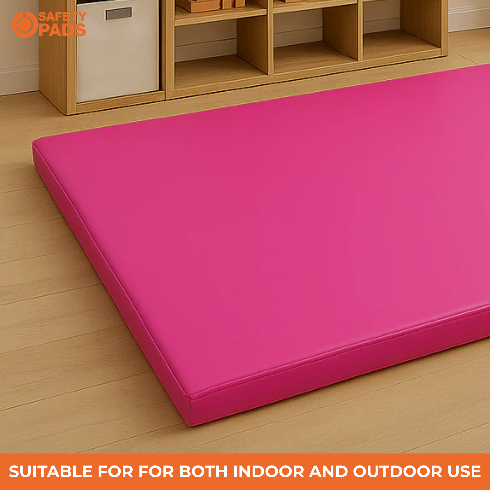 A bright pink rectangular foam safety pad placed on a light wood floor in a room setting, with a wooden storage shelf visible in the background. An orange banner at the bottom reads 'SUITABLE FOR BOTH INDOOR AND OUTDOOR USE', and the 'Safety Pads' brand logo appears in the top-left corner.